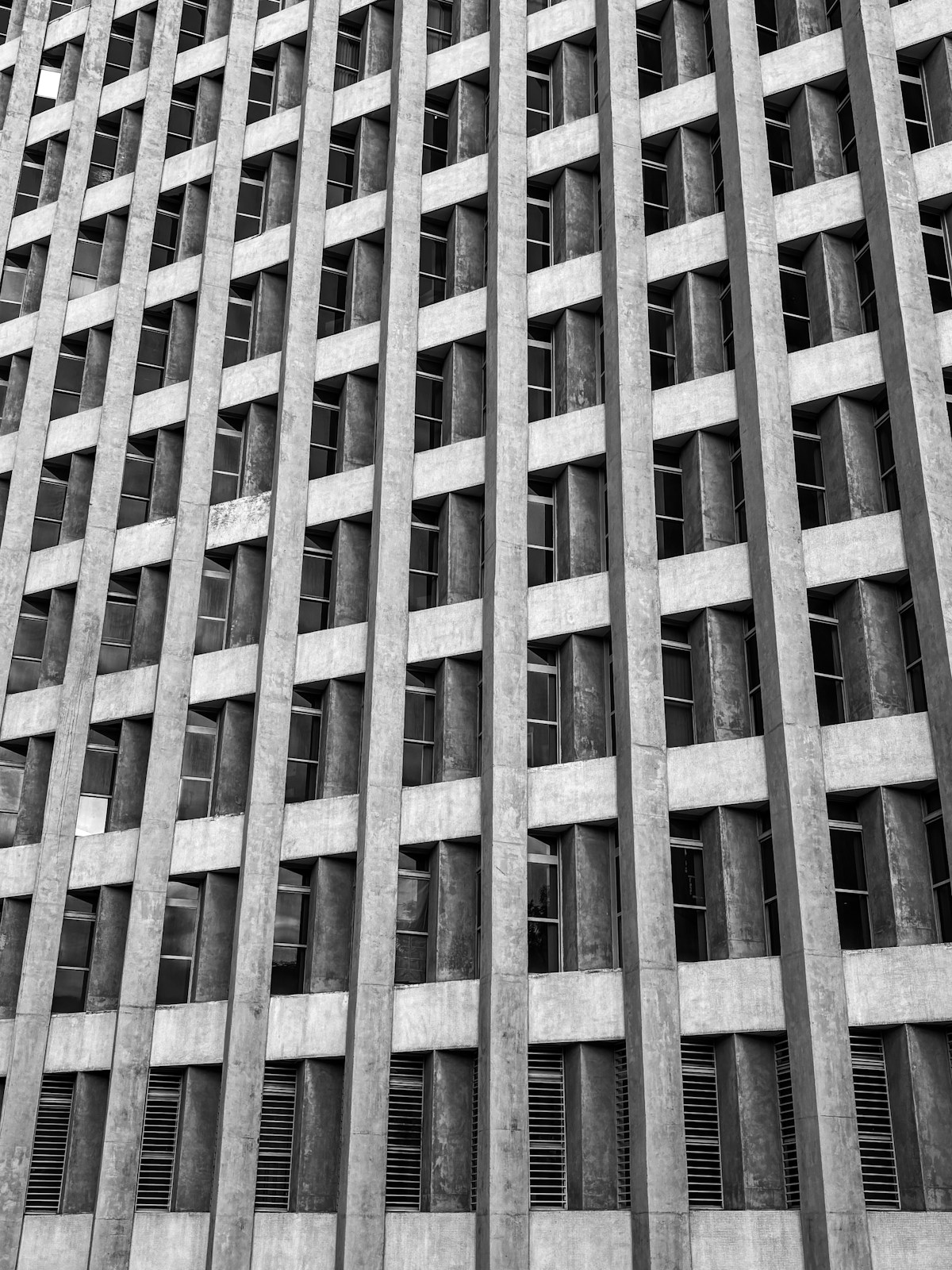 Dense grid of deep-set windows on a brutalist concrete facade — rhythm of voids and mass