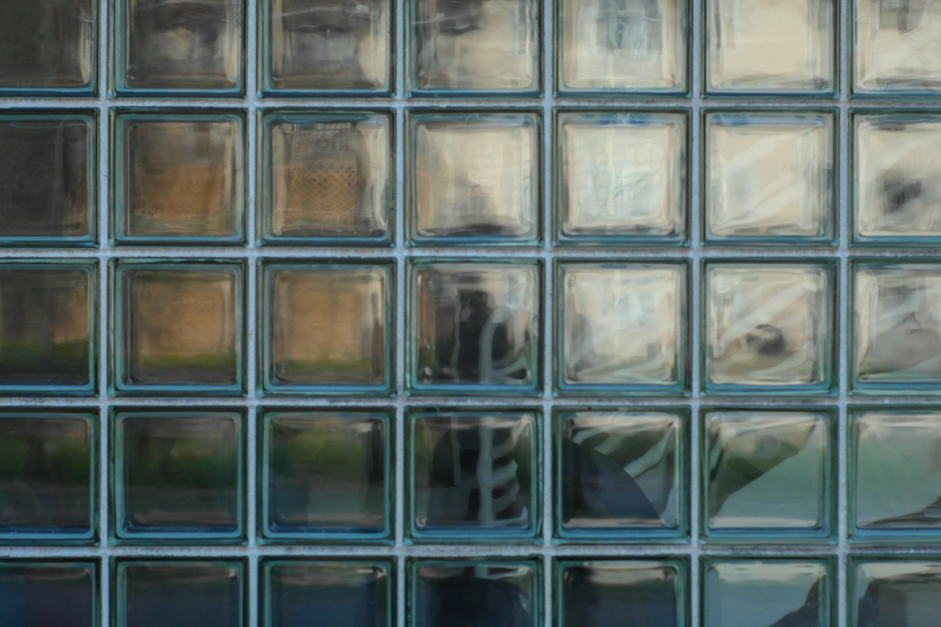 Close-up of glass block wall showing ghostly silhouette diffused through the translucent grid